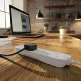 White power strip with multiple outlets on a wooden desk in a home office setting.